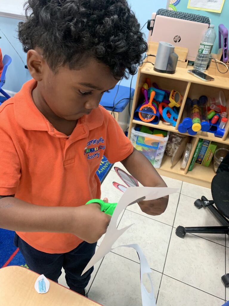 A preschooler in a Learningville uniform cutting out a paper craft with child-safe scissors